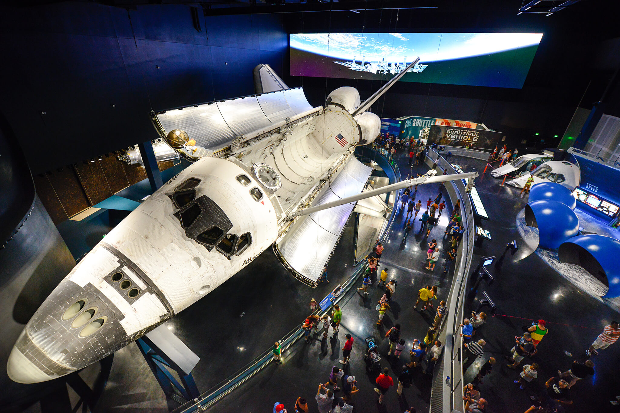 Visão aérea do ônibus espacial Atlantis em exposição no Kennedy Space Center, em Orlando, com visitantes ao redor apreciando a exibição.