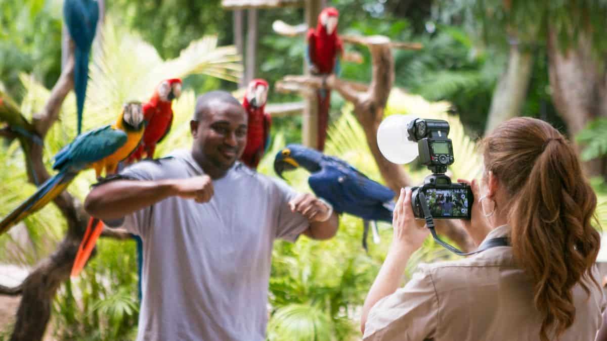 Crianças no Parrot Jungle Island em Miami, segurando aves exóticas em um ambiente tropical. Elas estão sorrindo e se divertindo enquanto interagem com os pássaros, criando uma experiência única e educativa, cercadas por vegetação exuberante e cores vibrantes.