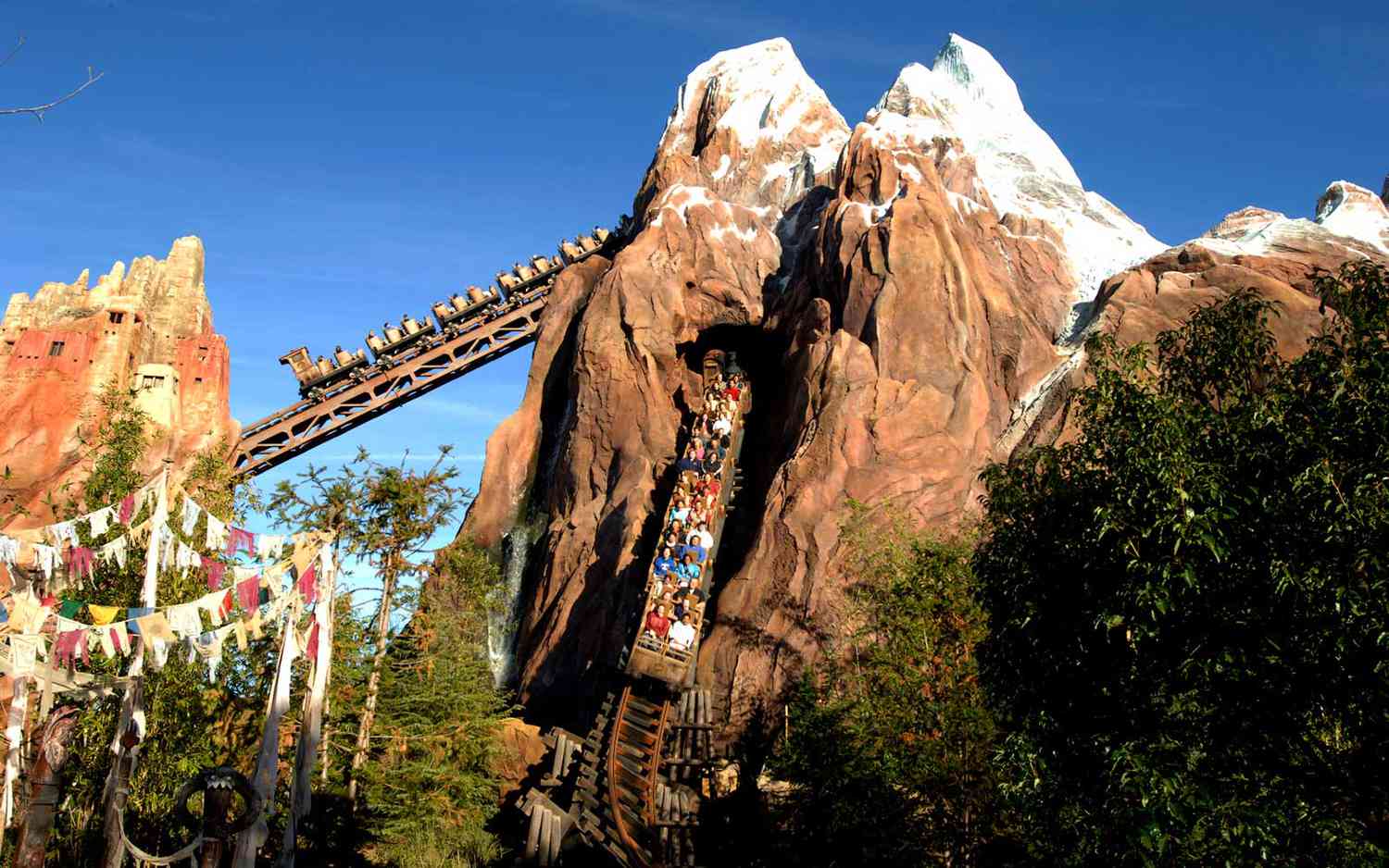 Montanha-russa Expedition Everest no Disney's Animal Kingdom em Orlando, com um trem cheio de visitantes descendo de uma montanha com neve, cercado por vegetação.