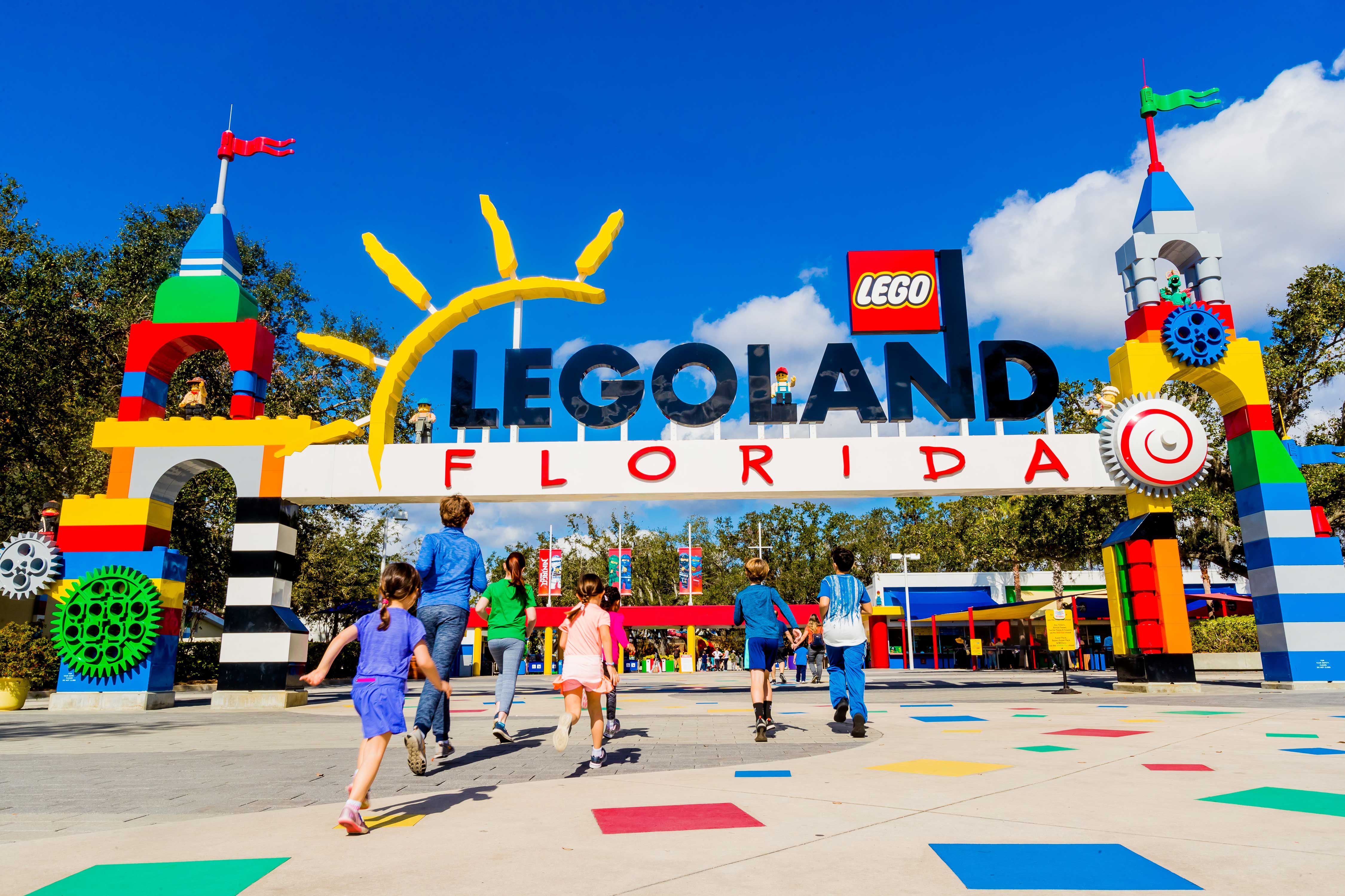 Crianças e famílias correndo em direção à entrada do Legoland Florida Resort, com a estrutura de arco colorida e temática de LEGO destacando o parque como um lugar divertido e alegre para crianças.