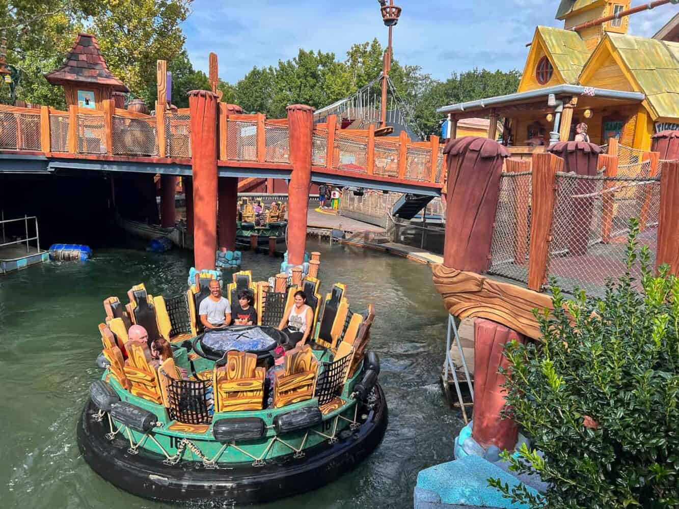 Grupo de pessoas a bordo da atração Popeye & Bluto's Bilge-Rat Barges no Islands of Adventure, em Orlando, enquanto atravessam uma corredeira cercada por uma temática de cais e barcos de madeira.