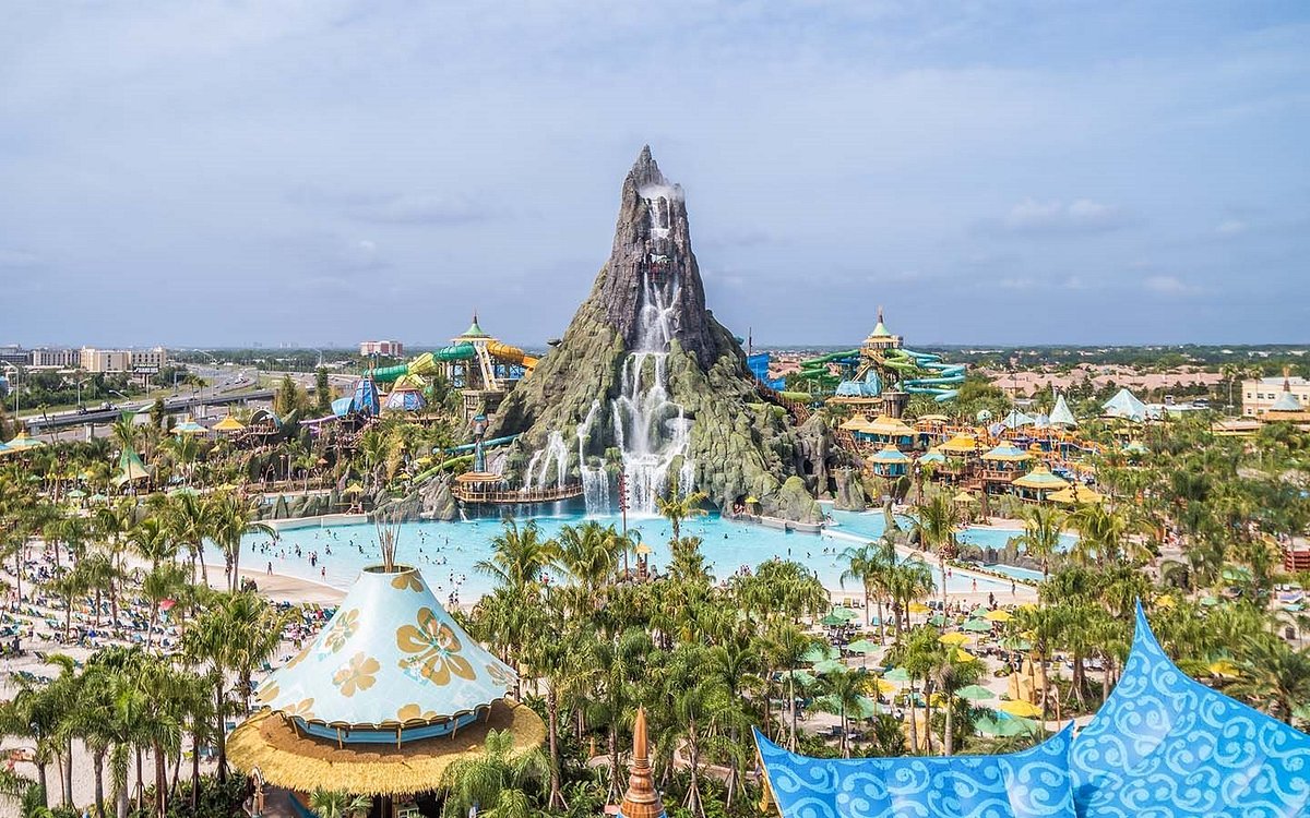 Parque aquático Volcano Bay em Orlando, apresentando um grande vulcão com toboáguas que se estendem de sua base, rodeado por uma ampla área de piscina e visitantes aproveitando o sol.